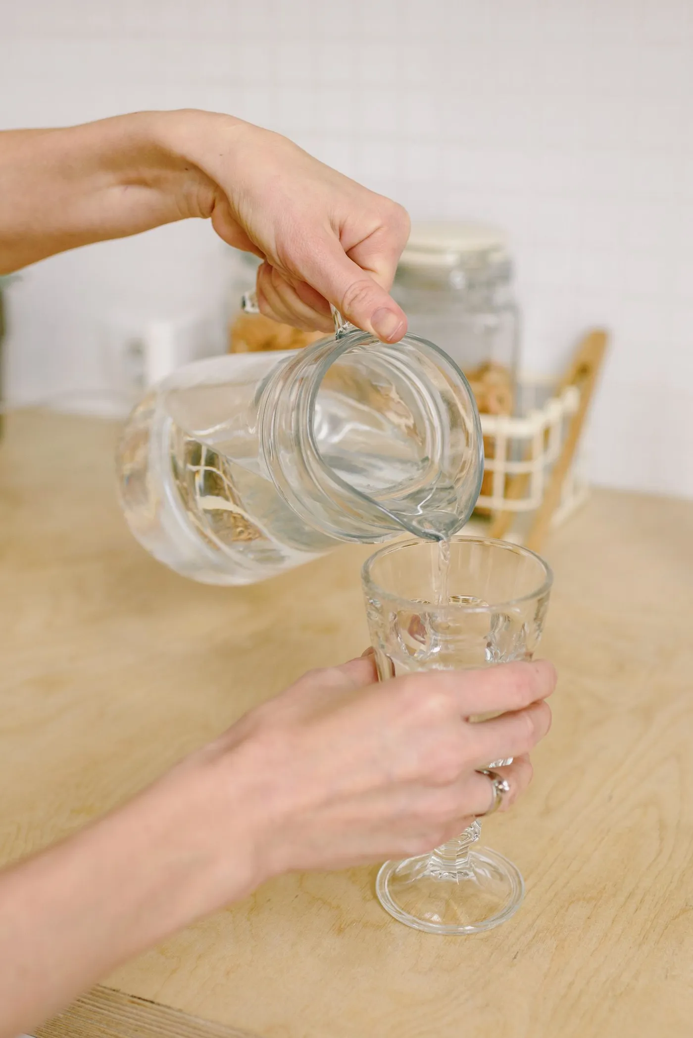 Hands pouring fresh water from a pitcher into a drinking glass