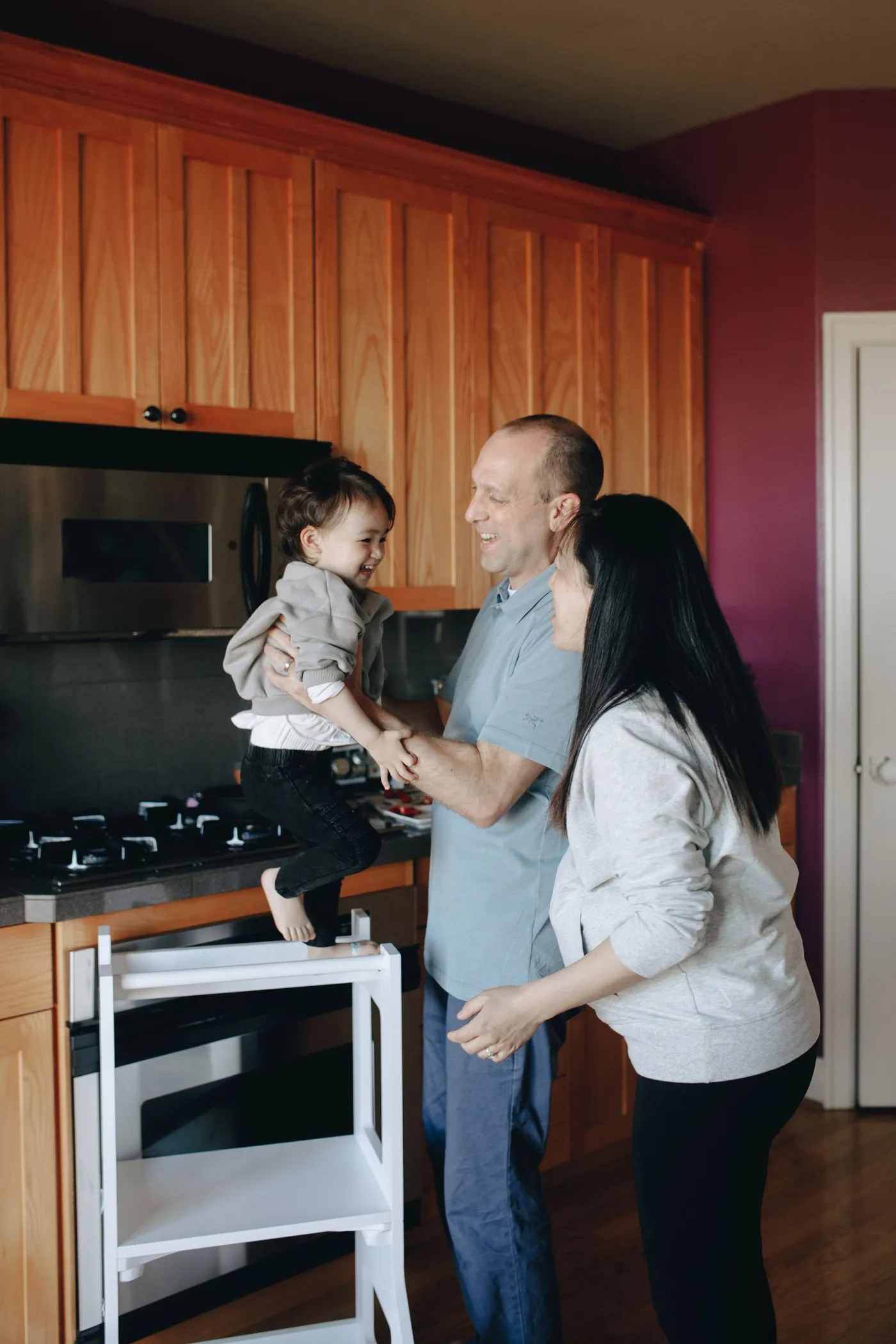 Parents laughing with their toddler standing at the kitchen stove